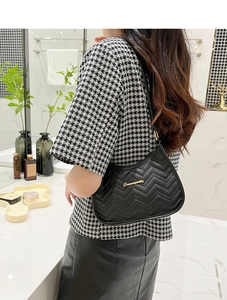 Detail of black chevron quilted shoulder bag featuring gold logo and sleek metal zipper