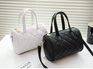 Close-up of quilted cylinder Boston handbags in black and white with gold zipper details