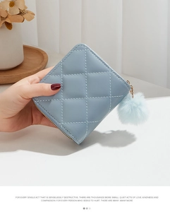 Détail du porte-monnaie matelassé bleu clair avec logo en métal, zip doré et pompon doux
