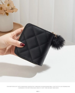 Vue détaillée du portefeuille matelassé noir avec zip doré et pendentif pompon en fourrure