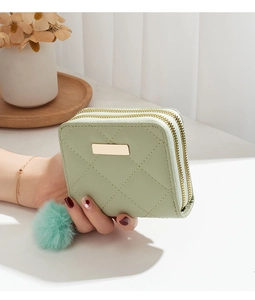 Détail d'une pochette vert clair matelassée avec double zip et pendentif pompon doux