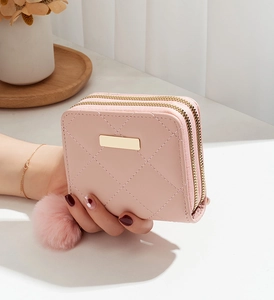 Détail du portefeuille rose matelassé avec double fermeture éclair et pompon décoratif