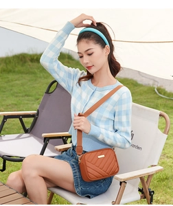 Brown quilted crossbody camera bag with adjustable strap in an outdoor camping setting