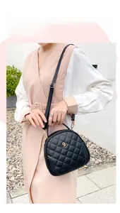 Detail of black quilted shoulder bag with golden floral logo shown on model outdoors
