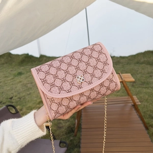 Pink crossbody chain bag with clover pattern and golden flower buckle on outdoor grass