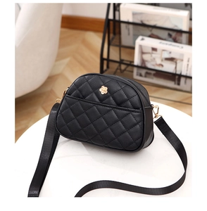 Detail of black quilted shoulder bag featuring golden camellia logo and nylon strap