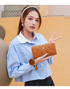 Close-up of brown quilted faux leather long wallet with pompom and gold floral detail