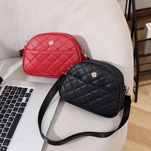 Quilted shell crossbody bags in red and black with flower logo on a grey sofa