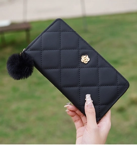 Detail of black quilted leather long wallet featuring golden flower clasp and pom pom charm
