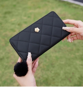 Detail of black quilted leather wallet with gold camellia accent and pompom charm