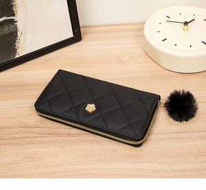 Detail of black quilted leather long wallet featuring gold flower logo and faux fur pompom