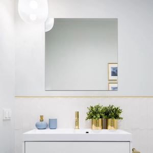 Detail of square frameless wall mirror in a modern bathroom with gold faucet