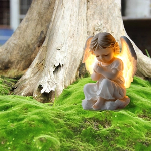Luminous praying angel garden ornament with glowing wings on green mossy ground