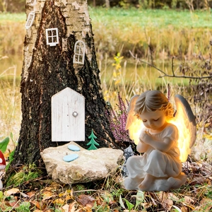Luminous angel garden ornament with glowing wings placed by a tree trunk outdoors