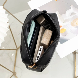 Black quilted crossbody bag with golden zipper on marble background and daily essentials