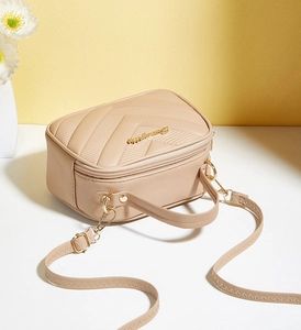 Detail of beige chevron quilted bag with gold logo and adjustable shoulder strap