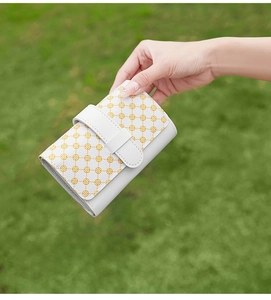 Detailed close-up of compact white and yellow clover pattern wallet held outdoors