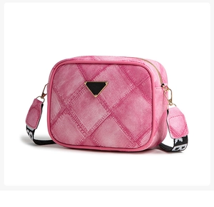 Detail view of pink denim texture camera bag with triangle metal logo and wide strap
