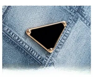 Close-up of golden triangle metal hardware on blue denim crossbody square bag