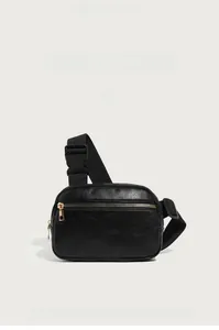 Detail of black pebbled leather texture with golden metal zipper on a crossbody chest bag