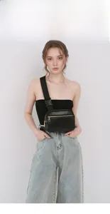 Close-up of black crossbody chest bag with gold zippers and adjustable strap on model