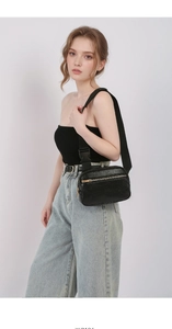 Detail of black pebbled leather crossbody chest bag with golden zippers and adjustable strap