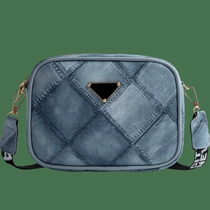 Denim patchwork crossbody bag with diamond quilting and wide logo strap on green backdrop