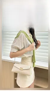 Detail of cream-colored leather crossbody bag with gold chain and metal buckle on a model