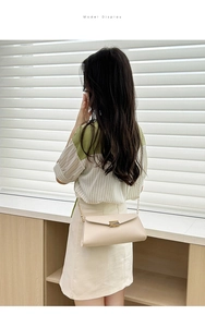 Detailed back view of a beige envelope chain bag with metallic clasp on a model