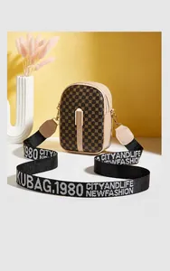 Detail of checkered crossbody bag with lettered strap and gold zipper on a warm background