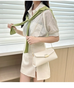 Detail of a creamy white envelope crossbody bag with gold lock and chain strap on model