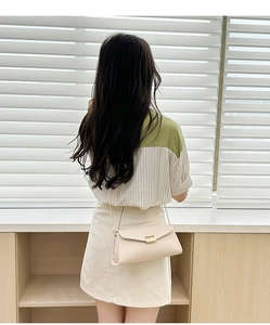 Detail of minimalist cream flap bag with gold chain strap on a matching skirt and top