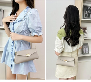 Detail of light gray envelope crossbody bag with gold chain strap and metal lock
