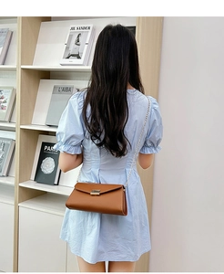 Brown leather envelope chain bag styled on model with light blue dress in a modern room