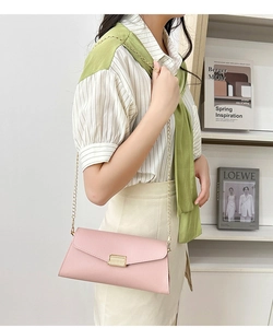 Pink envelope chain bag with lychee texture and gold clasp worn by a model in a room