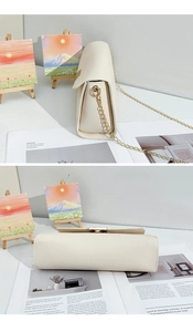 Close-up of litchi texture leather surface and golden metal chain of the cream shoulder bag