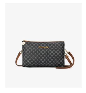 Detail of printed crossbody bag featuring golden logo and brown leather strap accents
