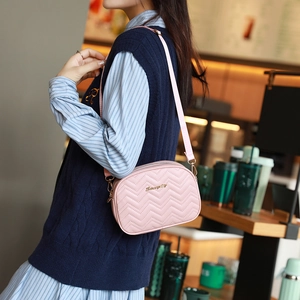 Sac bandoulière rose matelassé avec broderie ondulée et logo doré dans un café