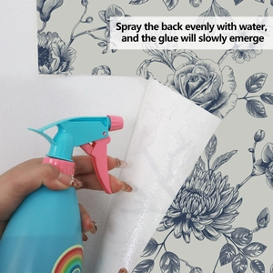 Close-up showing how to spray water on the back of blue floral wallpaper to activate glue
