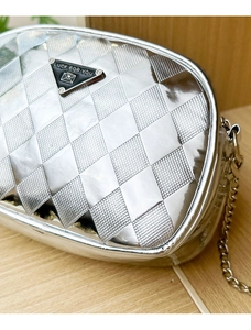 Détail macro du sac à bandoulière argenté matelassé avec plaque triangle et chaîne