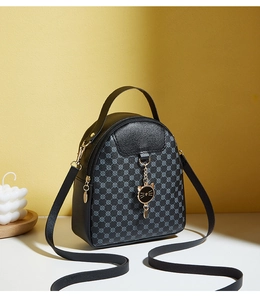 Mini black crossbody bag with cat charm detail and monogram print on warm background