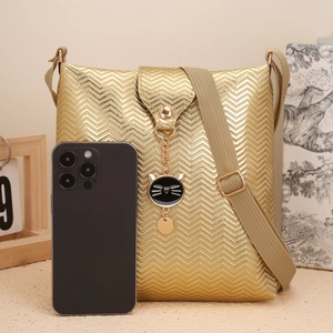 Détail du sac bandoulière doré à motif chevron avec charme chat et sangle en tissu