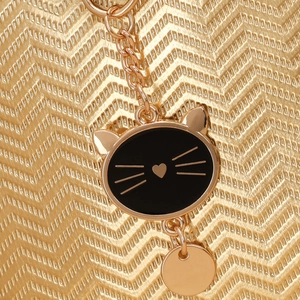 Détail du sac doré texturé avec un pendentif chat noir et une décoration de cœur