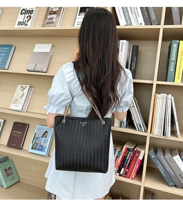 Detalle de bolso shopper trenzado negro con cadena dorada y placa metálica con logotipo