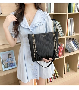 Detalle del bolso tote tejido negro con logotipo triangular y correa de cadena dorada