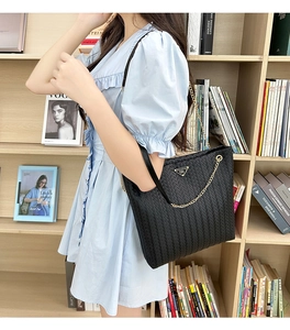 Primer plano de bolso tote negro de cuero trenzado con cadena dorada y placa de metal