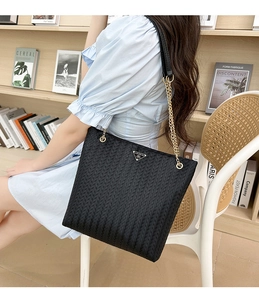 Detalle del bolso tote negro trenzado con correa de cadena dorada y placa de metal