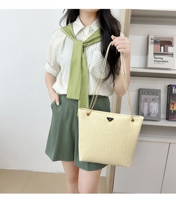 Detalle de bolso tote tejido beige con asas de cadena metálica y logo triangular