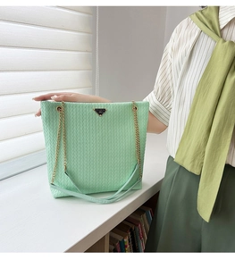 Detalle de bolso tote verde claro con textura tejida, cadena dorada y emblema