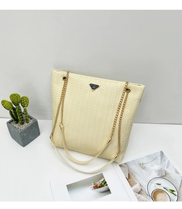 Detalle de bolso tote tejido beige con diseño de espiga y correa de cadena dorada